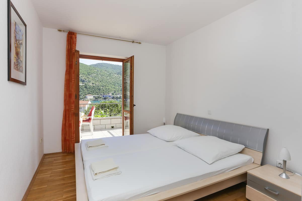 A bedroom with a bed, a nightstand, and a view of a balcony with a chair.