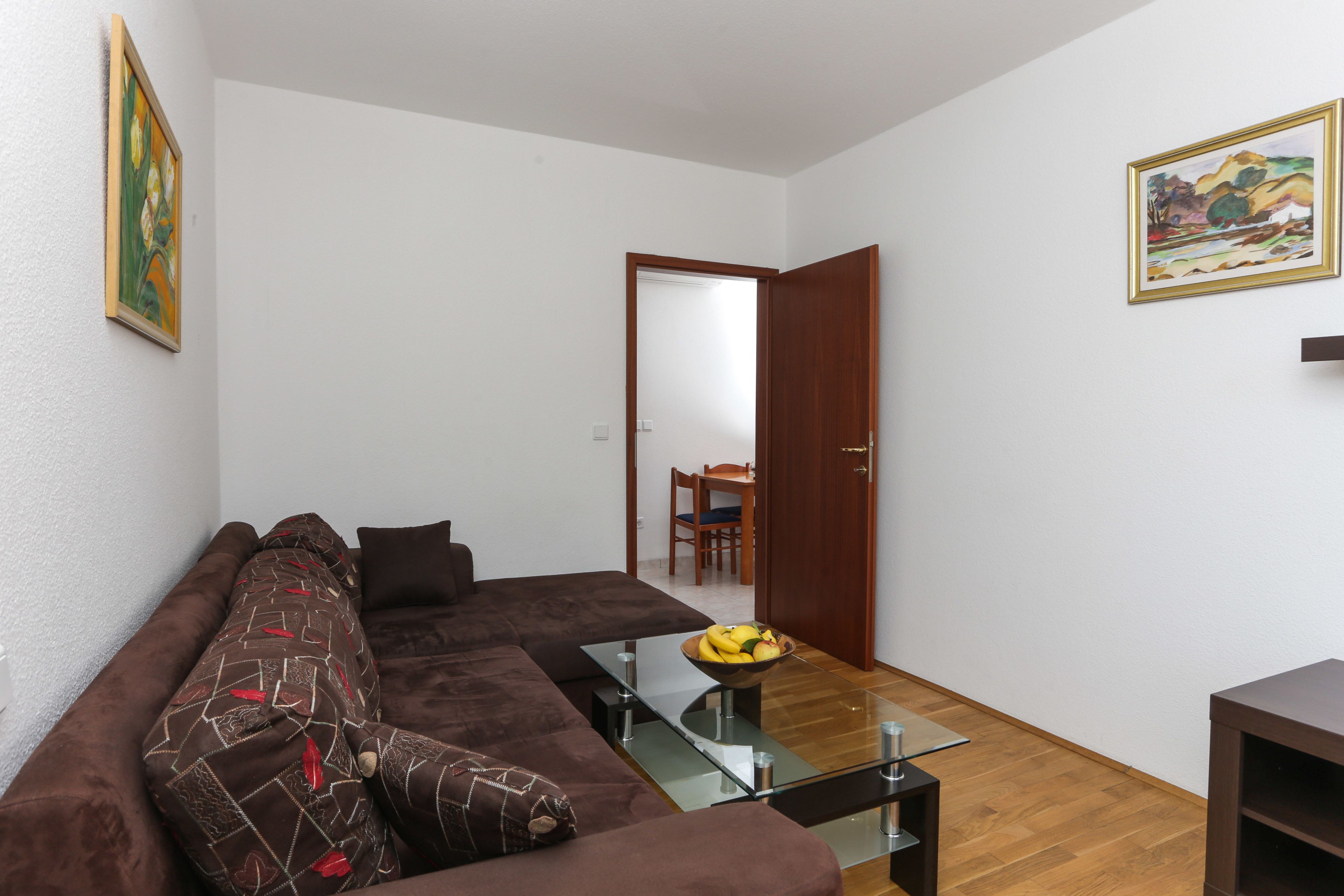 A living room with a brown sofa, a glass coffee table, and a painting on the wall.