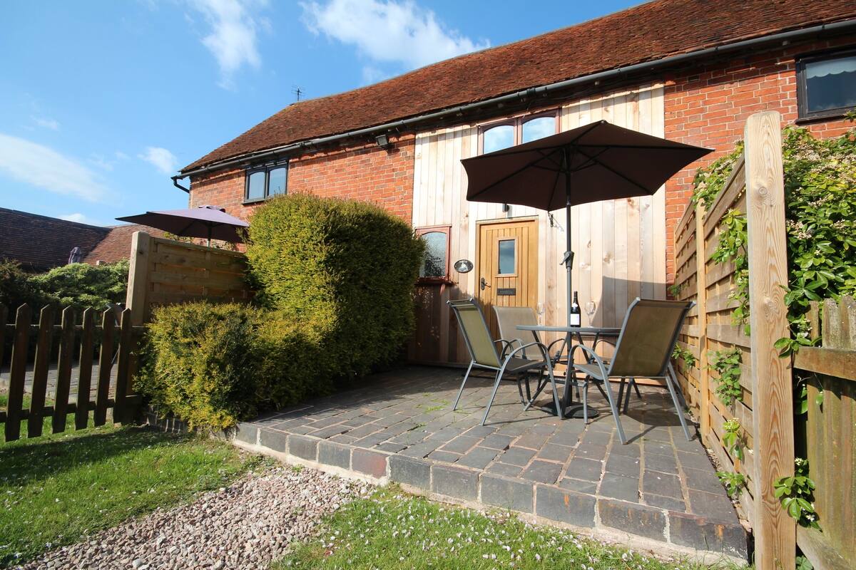 A brick house with a patio area featuring a table and chairs, a wooden fence, and a wooden door.