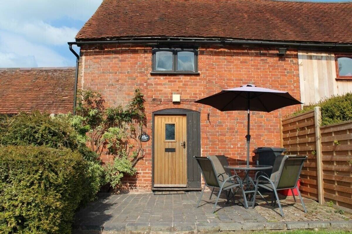 A brick house with a wooden door, a small window, and a patio with a table and chairs.
