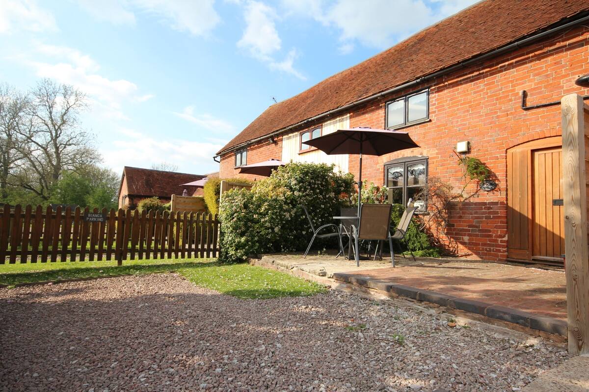 A brick house with a gravel driveway, a wooden fence, and a patio area with outdoor furniture and an umbrella.