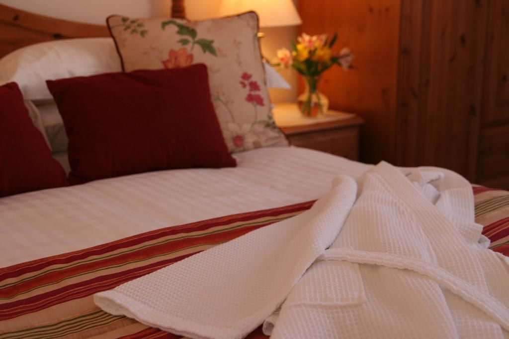 Uma cama bem arrumada com colcha listrada, um travesseiro vermelho e um roupão branco ao lado.
