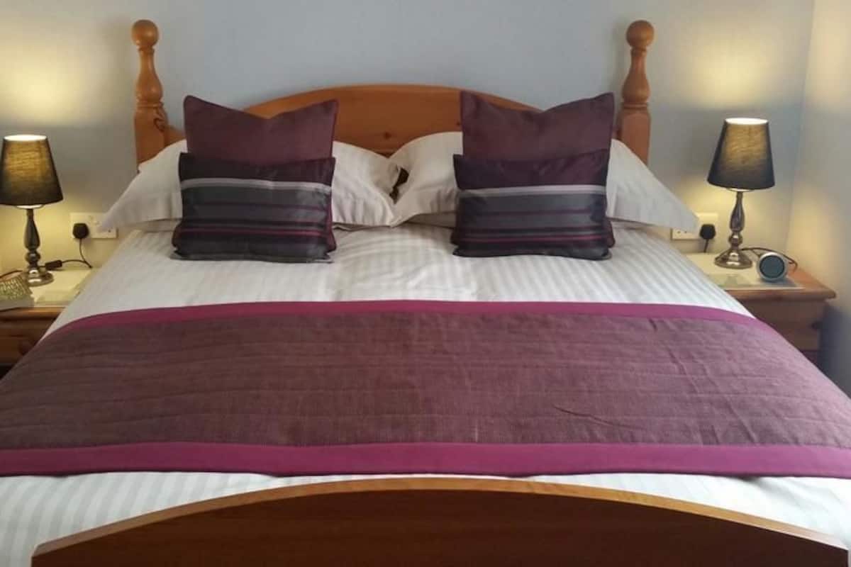A neatly made bed with a wooden headboard, two bedside lamps, and a purple throw blanket.