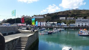 A harbor with boats docked, stone steps leading down to the water, and buildings in the background. - Mandeley Guest House (Helston)