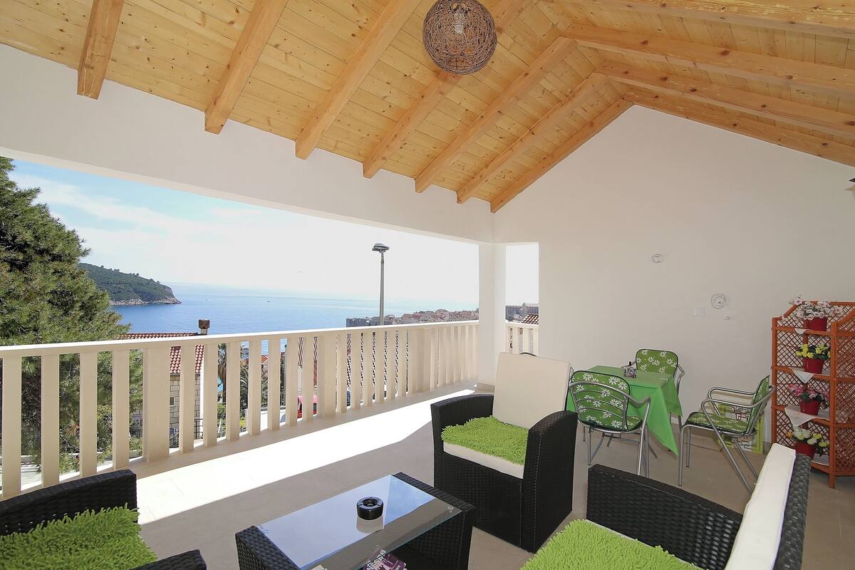 A balcony with a wooden ceiling, a table, chairs, and a view of the sea.