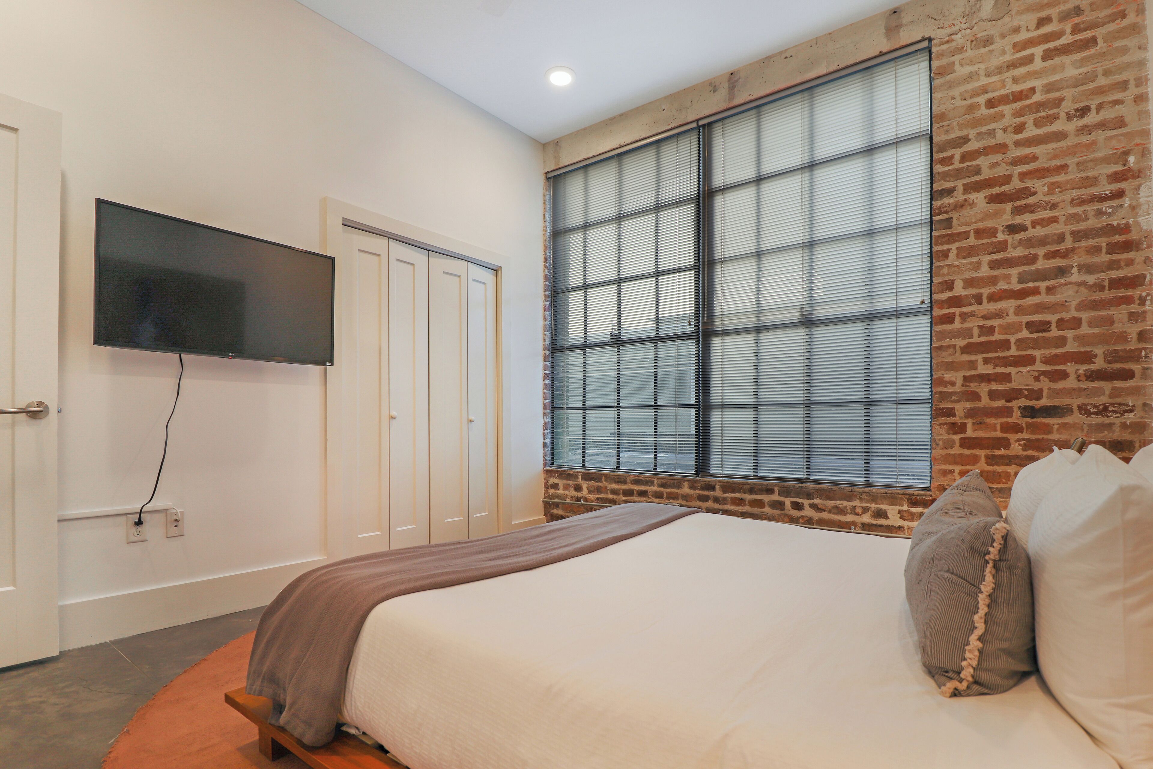 Ein Schlafzimmer mit einem großen Bett, einem an der Wand befestigten Fernseher und einem Fenster mit Jalousien.