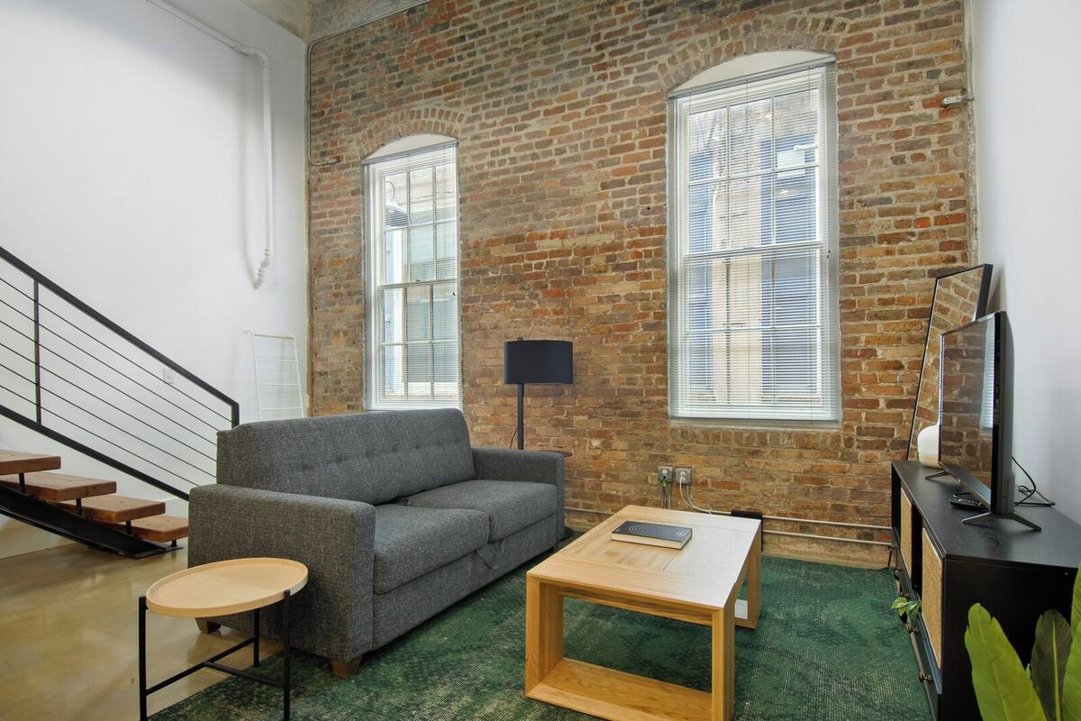 A modern living room with a brick wall, a grey sofa, a wooden coffee table, and a TV on a stand.