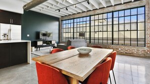 A modern kitchen with a large window, a dining area with a wooden table and red chairs, and a visible kitchen counter with appliances. - Roami at Motorworks (New Orleans)