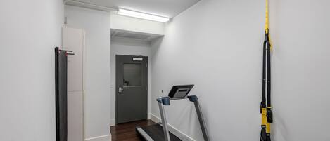 A hallway with a treadmill, a measuring tape, and a door leading to another room.