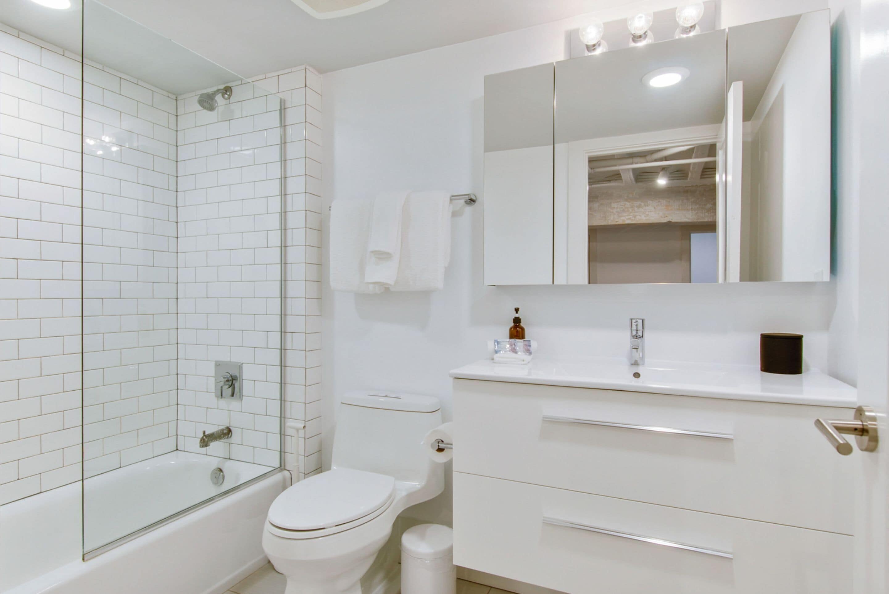 A modern bathroom with a glass-enclosed shower, a white toilet, and a vanity with a mirror and storage drawers.