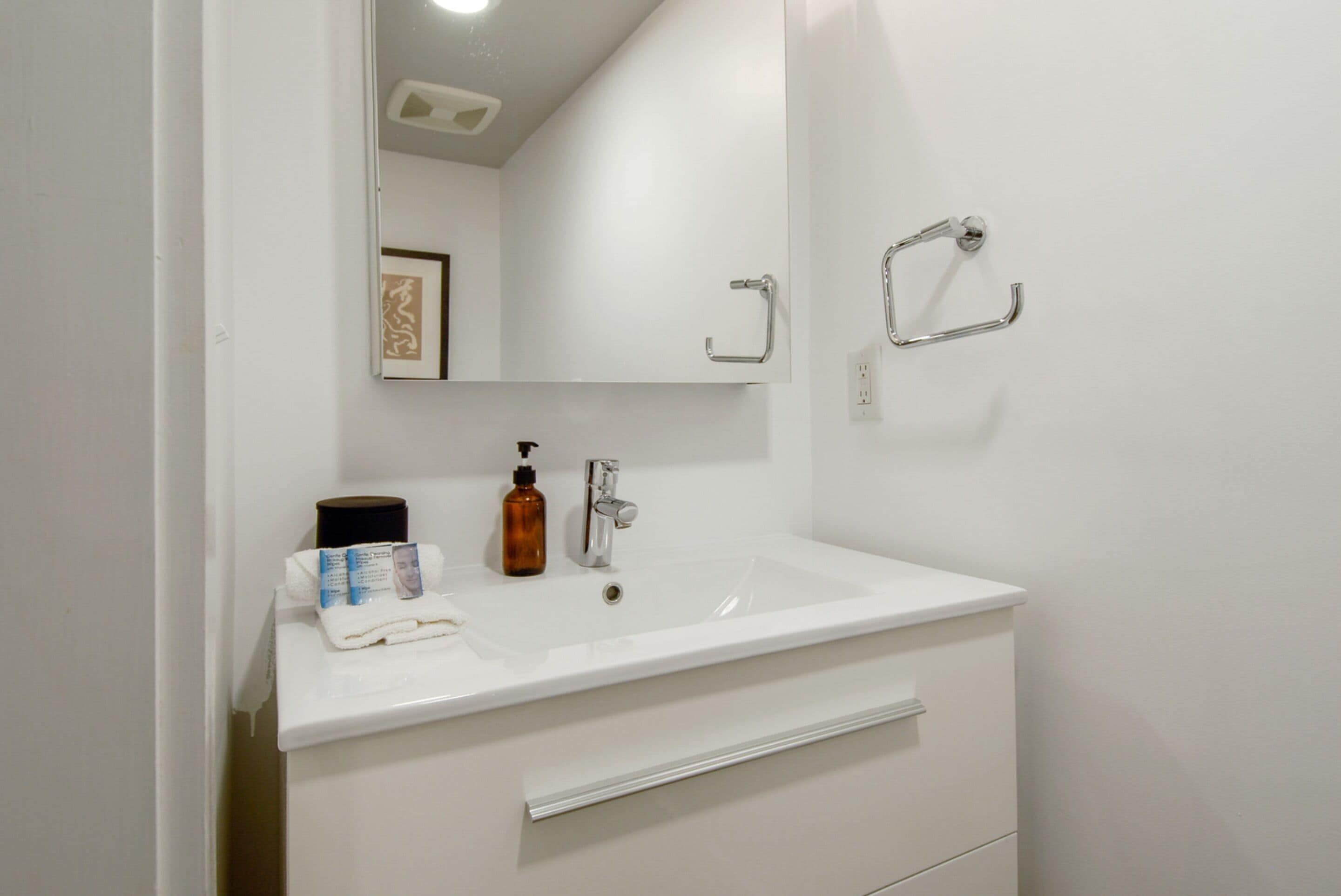 A white bathroom with a sink, mirror, and towel rack.