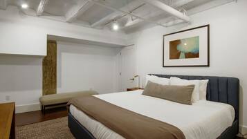 A modern bedroom with a large bed, a bench, a nightstand, and a framed picture on the wall.