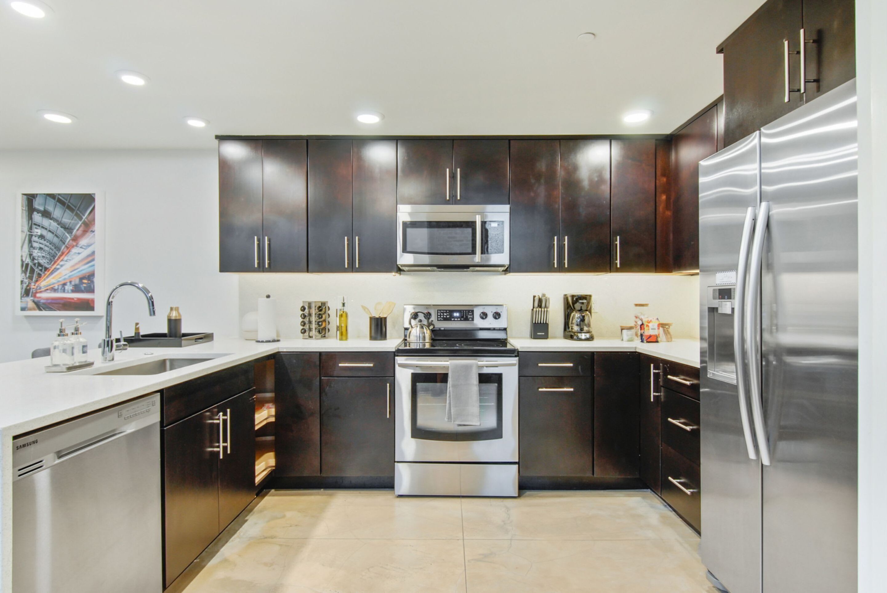 Una cocina moderna con electrodomésticos de acero inoxidable, armarios oscuros y piso de baldosas.
