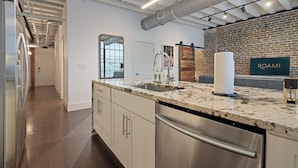 A modern kitchen with stainless steel appliances, a marble countertop, and a brick accent wall. - Roami at Motorworks (New Orleans)