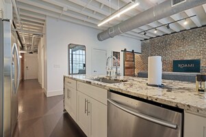 Una cocina moderna con electrodomésticos de acero inoxidable, encimera de mármol y pared de ladrillo decorativa.