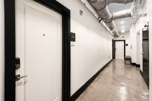 A hallway with a white door, a number sign, and a bench. - Roami at Motorworks (New Orleans)