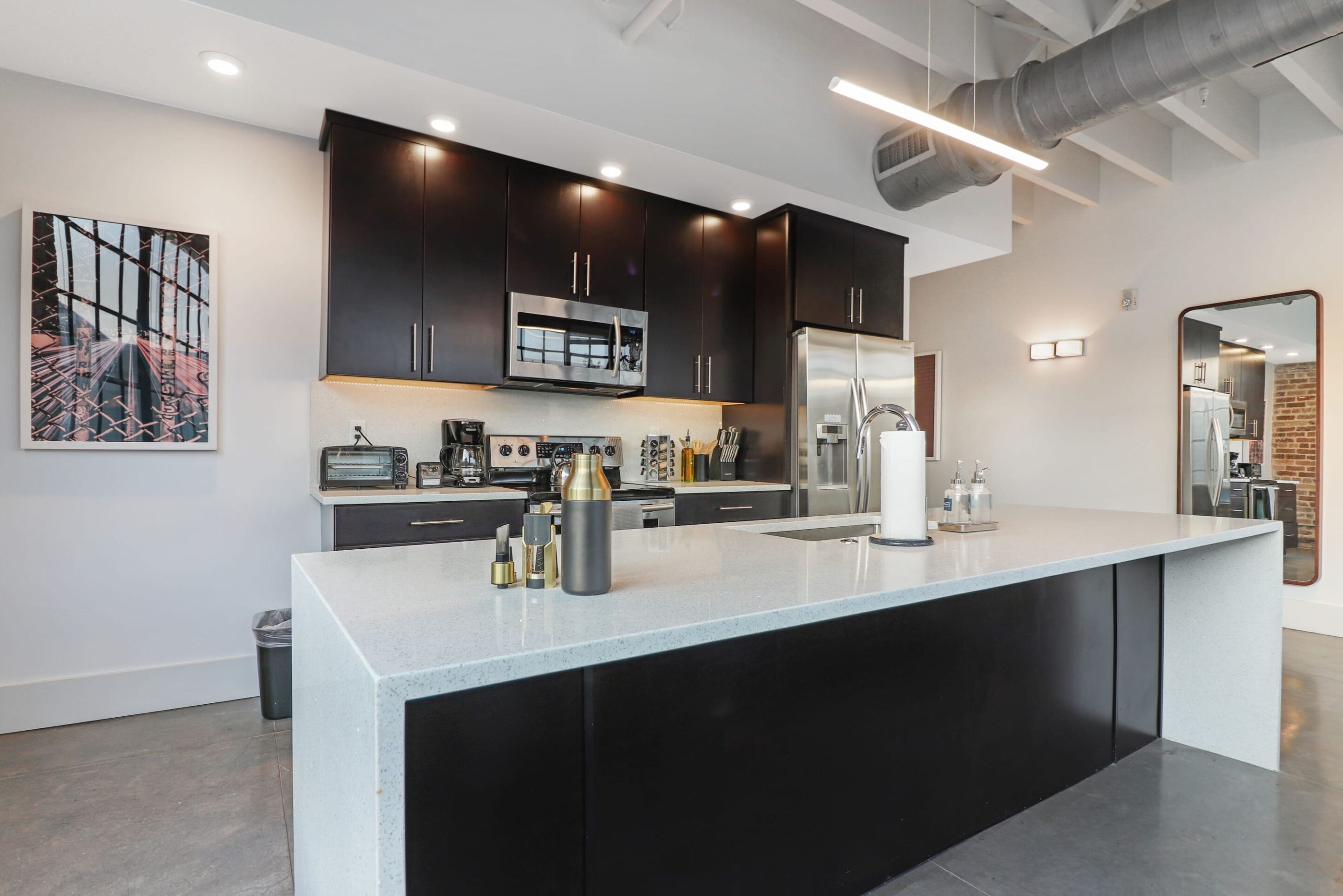 A modern kitchen with dark cabinets, stainless steel appliances, and a large island.