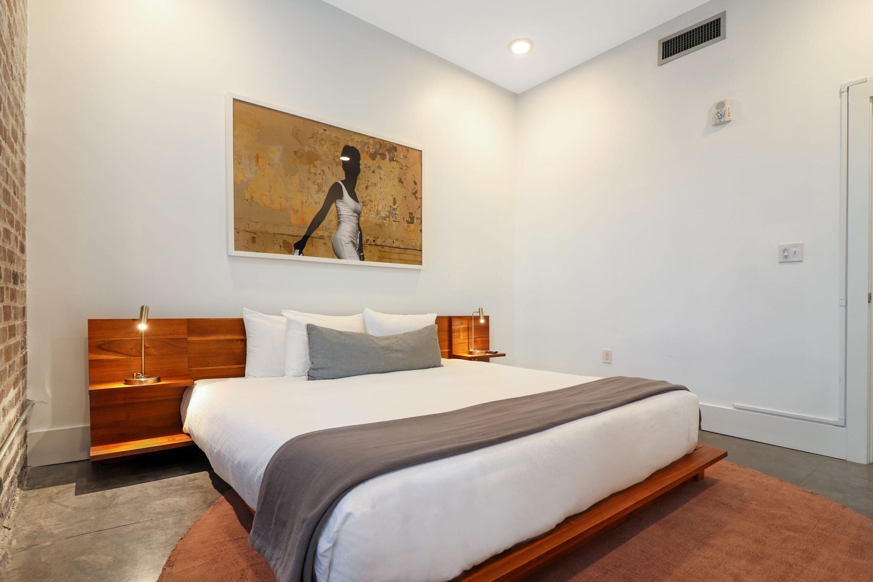 Una habitación de hotel moderna con una cama grande, cabecero de madera y un cuadro en la pared.