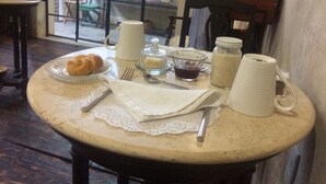 Une table de petit-déjeuner avec des croissants, des tasses de café, un pot à beurre, un bocal de confiture et un pichet de lait.