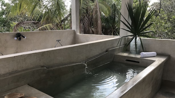 Un espace spa comprenant une grande piscine rectangulaire, trois bassins en bois, une serviette blanche et une plante.