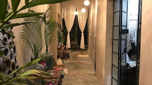 Un couloir étroit avec un banc en bois, des plantes en pot et un sol en béton.