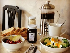 A breakfast setting with toast, a bowl of fruit, a bottle of jam, a coffee maker, and a cup.