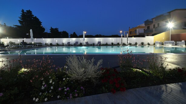 A swimming pool with lounge chairs and a white fence, surrounded by flowers and illuminated by street lamps. - Villa Luigia Luxury Relais (Gallipoli)