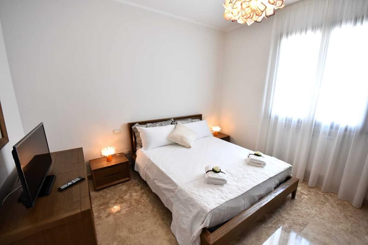 Une chambre d’hôtel avec un lit, des tables de chevet, une télévision et une grande fenêtre avec des rideaux.