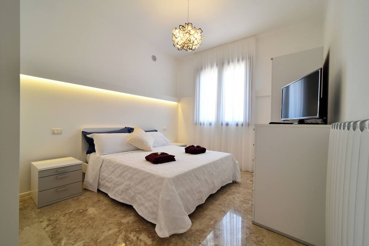 Une chambre d’hôtel moderne équipée d’un lit, d’une table de chevet, d’une télévision et d’un lustre original.
