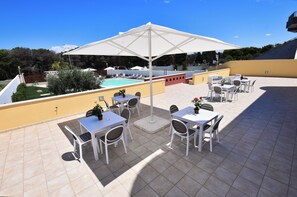 Terraza en la azotea con mobiliario exterior, piscina y una gran sombrilla que da sombra.
