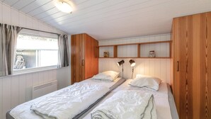 Quarto com duas camas de solteiro, painéis de madeira, janela com cortinas e uma estante com objetos decorativos.
