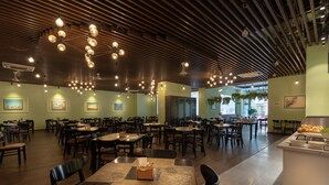 En rymlig restaurang med träribbor i taket, hängande lampor och ett centralt placerat sittområde med bord och stolar.