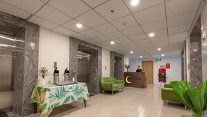 En hotellobby med väggar i marmor, en receptionsdisk, en grön soffa och ett bord med ett bordsskydd prytt med tropiska blad.
