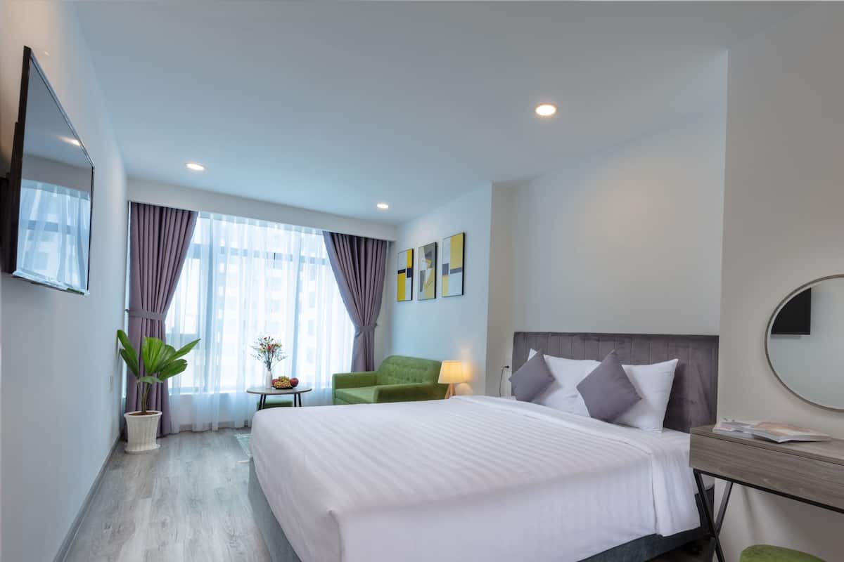 Quarto de hotel moderno com uma cama grande, uma escrivaninha, uma cadeira, uma planta em vaso e obras de arte nas paredes.