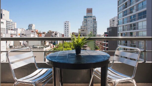 A balcony with a round table and two chairs, a potted plant, and a cityscape view. - Departamento Palermo con Balcon (Buenos Aires)