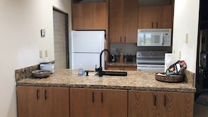 Una cocina con armarios de madera, encimera de granito, refrigerador, microondas y un lavamanos.