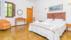 Ein Schlafzimmer mit Bett, Sessel, Schreibtisch, einer Tür, einem Feuerlöscher und einem Bild an der Wand.