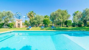 Ein Swimmingpool mit einem Windrad im Hintergrund, umgeben von Bäumen und einer Rasenfläche.