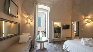 A hotel room with a bed, a seating area with cushions, a small table with decorative items, a television, and wall-mounted lighting. - Al Console Luxury Suite (Monopoli)