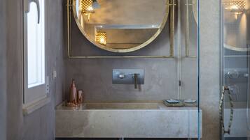 A modern bathroom with a round mirror, a glass shower enclosure, and a small vanity area.