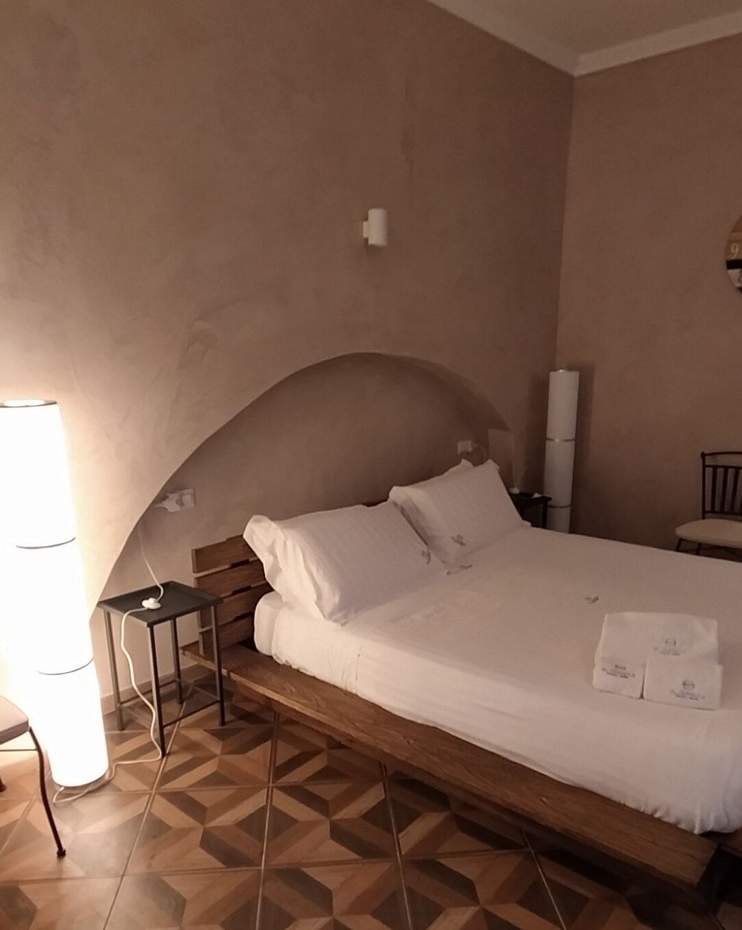 Un dormitorio con cama de madera, ropa de cama blanca, una mesita de noche pequeña y una lámpara.
