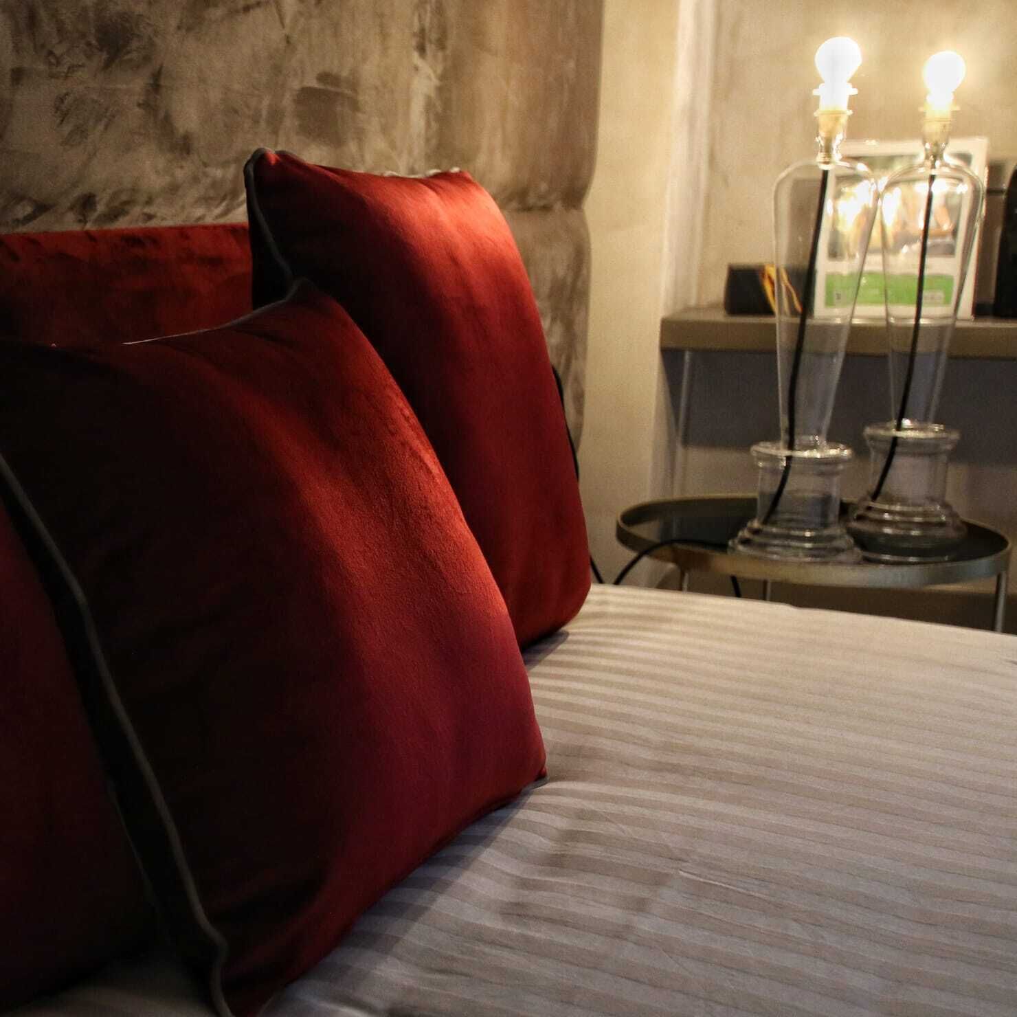 A bed with red pillows and a bedside table with a lamp and a bottle.