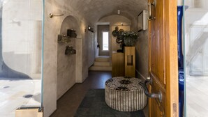 A narrow hallway with a wooden door, a patterned ottoman, and a staircase leading to another room. - Al Console Luxury Suite (Monopoli)