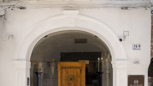 Entrada de un edificio con una puerta de madera, un arco de entrada y un cartel con la dirección.