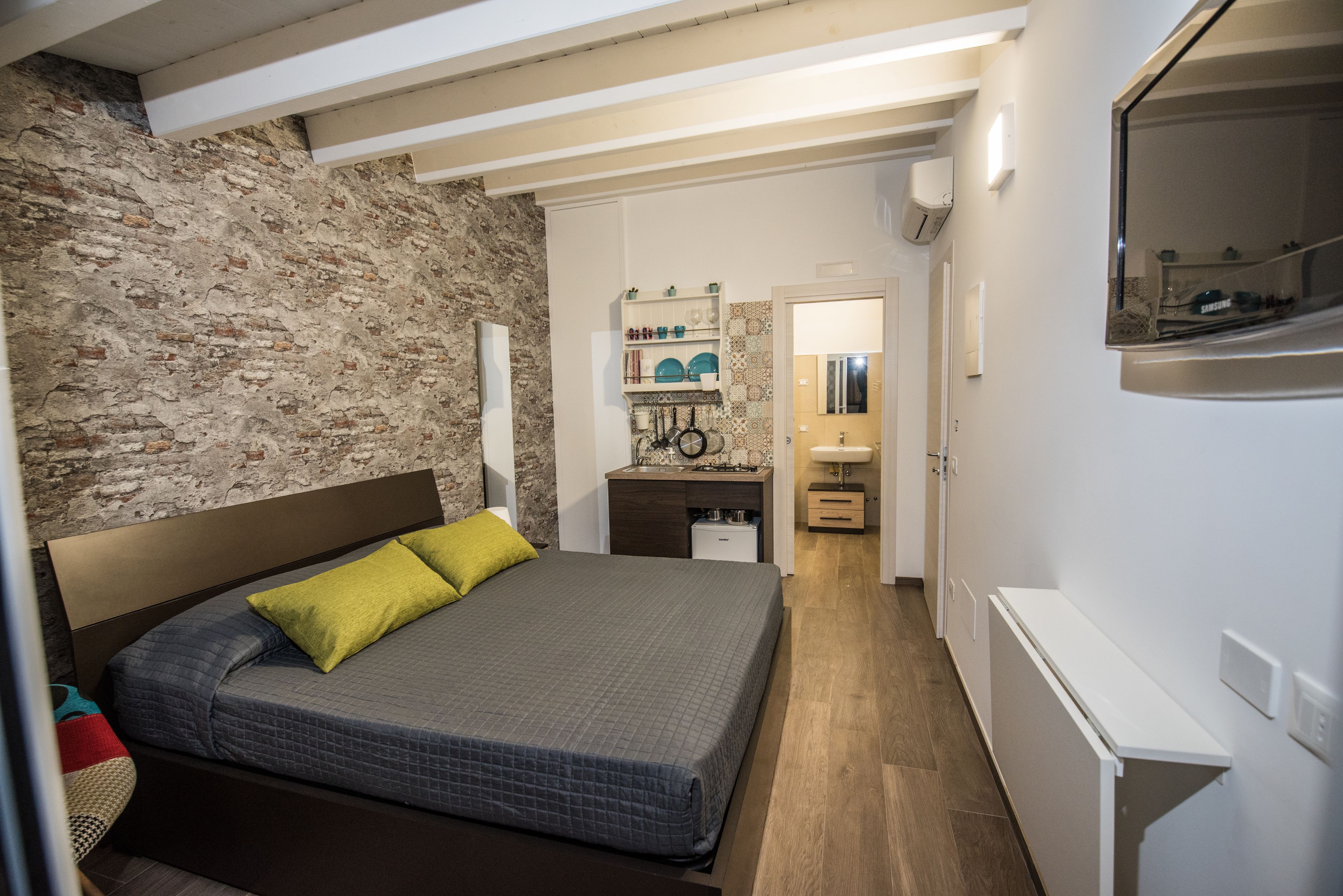 Un dormitorio con cama, mesita de noche, cómoda, espejo y pared de ladrillo.