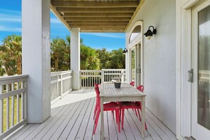 A covered outdoor patio with a white table and red chairs, surrounded by white railings and palm trees. - Heated Pool-Ocean Views-Steps to Beach (St. Augustine)