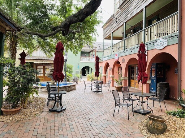 An outdoor patio with tables and chairs, a fountain, and a building with a balcony.