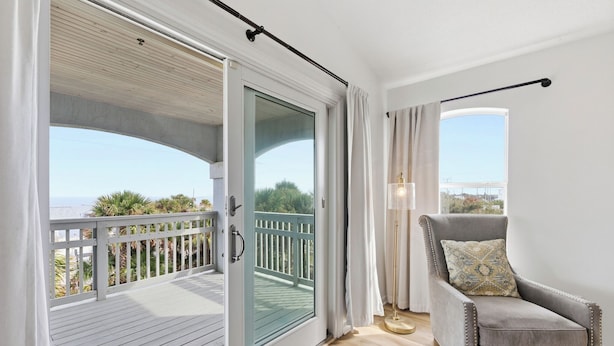 A room with a sliding glass door leading to a balcony, a grey armchair with a patterned pillow, and a floor lamp. - Vilano Beach Pool Home-Ocean Views (St. Augustine)