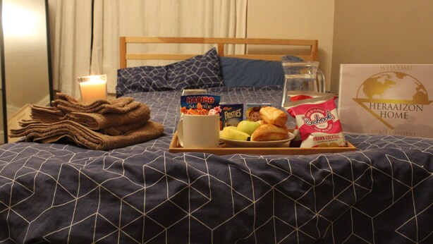 Un lit bien fait, avec un plateau contenant divers éléments pour le petit-déjeuner, notamment des croissants, une tasse et une boîte de collations.