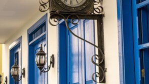 A clock mounted on a wall with blue doors and a white wall. - El reloj casa hotel (Filandia)
